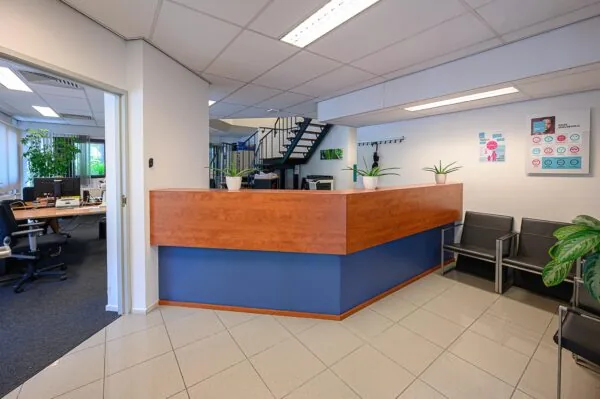 Receptiebalie met houten front, blauwe onderkant en drie planten in een modern kantoorinterieur bij De Linie.